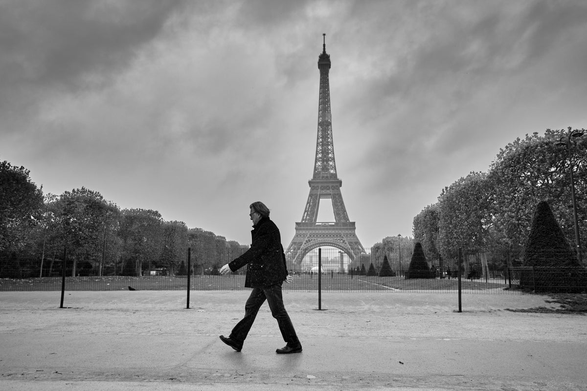 Man in a black coat walking toward the Eiffel Tower, black-and-white